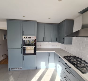Modern blue kitchen cabinets with white subway tile backsplash, built-in double oven, and gas hob.