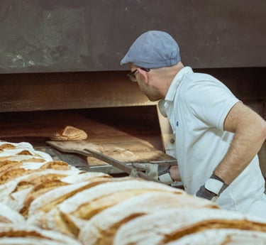 Panadero utilizando una pala de madera para hornear pan de masa madre en un horno tradicional