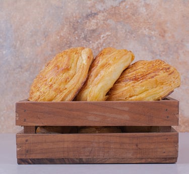 Hojaldres dorados y hojaldrados servidos en una caja rústica de madera sobre un fondo de piedra.