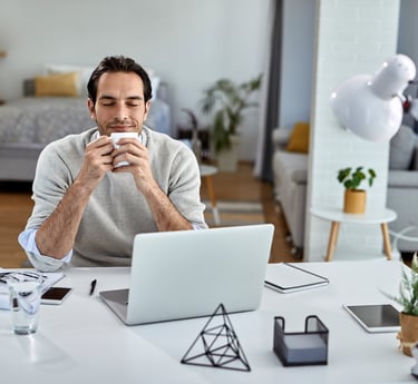 Hombre tomando una pausa mental con café frente a su laptop en home office,