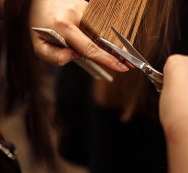Estilista profesional recortando cabello largo castaño con tijeras de salón y un peine.