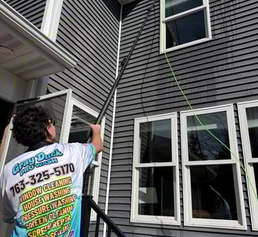 Gray Duck Pro Wash employee cleaning windows on a two-story home using a water-fed system.