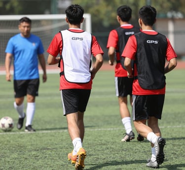 A dynamic football coach reviewing GPS tracker data with an athlete on the training pitch.
