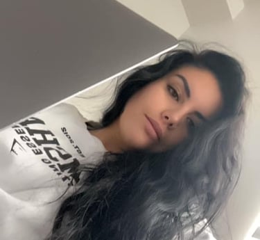 Young woman with long dark wavy hair wearing a white sweatshirt looking at a laptop computer.