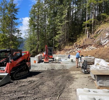 A worker using a Kubota skid steer and excavator to build a concrete block retaining wall.