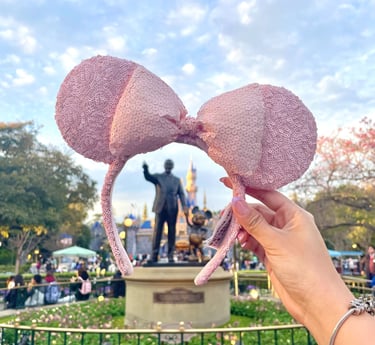 Mano sosteniendo orejitas de Minnie Mouse frente al castillo de Disneyland