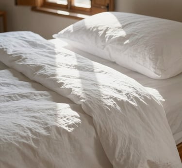 Crisp white linen sheets with natural creases, soft morning sun filtering through wooden shutters, throwing gentle shadows in a serene Provençal room.