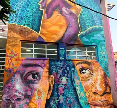 Vibrant outdoor street art mural featuring two diverse faces and joined hands on a brick building.