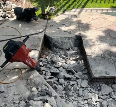 A red jack hammer in a pit of broken up concrete