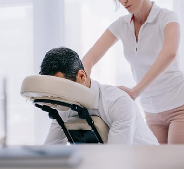 Professional massage therapist performing a seated chair massage for a businessman in an office.