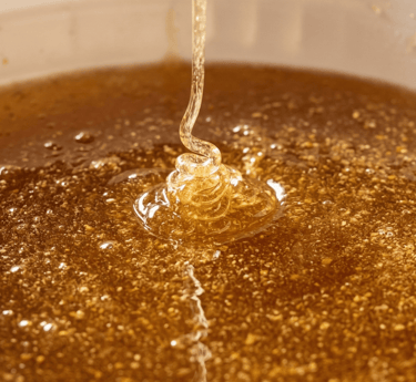 Golden raw honey pouring into a container, showing thick texture and air bubbles.