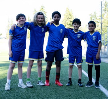 Young soccer players posing for a picture with arms on one another's shoulders.