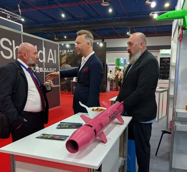 Tech professionals discuss military drone technology and pink missiles at an aerospace defense exhibition booth.