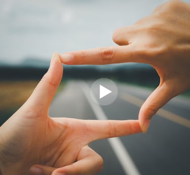 person's fingers making a rectangle with a "play" button in the middle against background of road