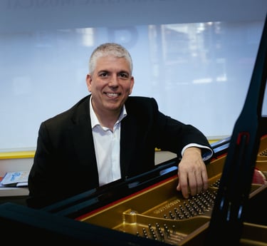 a man in a suit and tie smiling at the camera with baby grand piano