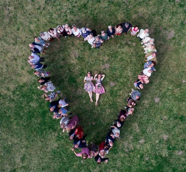 Hochzeitsgesellschaft formt Herz auf Wiese um liegendes Brautpaar. Drohnenaufnahme von Joel Pingel.