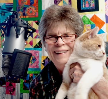Diane Lalomia, the artist  is holding her cat, Honey with a quilt top with cats & dogs, Diane pieced