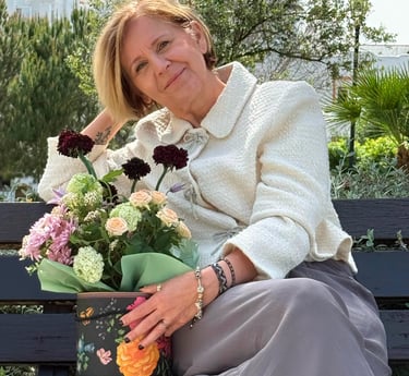 Violeta smiling sits on a park bench next to a decorative box filled with a colorful bouquet of flowers
