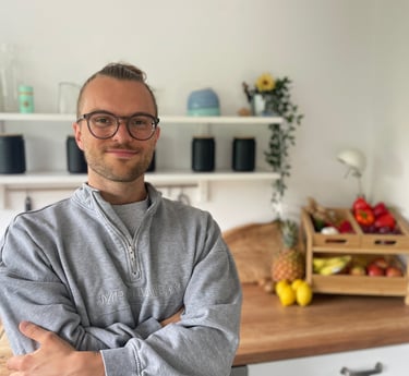 ein mann mit Brille und bart, der lächelnd in einer Küche steht vor Obst und Gemüse