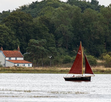 a sailboat in the water with a house in the background taken by Pixel Perfect Photography