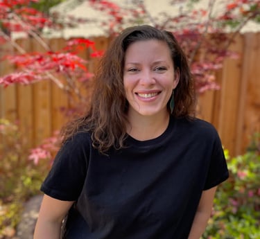 female author in a black shirt and jeans standing in front of a fence