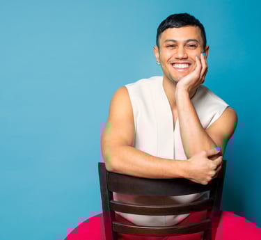 Founder sitting on a reversed brown chair. They are smiling and wearing a short-sleeve offwhite top.
