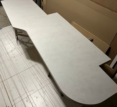 Custom white marble laminate countertop with a curved edge being fabricated in a workshop.