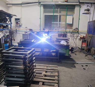 Professional welder in protective gear welding metal frames in an industrial workshop.