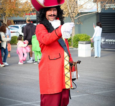 A man in a Captain Hook costume with a red coat and feathered hat at an outdoor event.