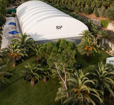 Aerial view of a large white event tent and lounge area surrounded by lush palm trees.