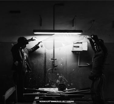 Du filmavimo komandos nariai montuoja apšvietimo įrangą nespalvoto muzikinio vaizdo klipo gamybai.