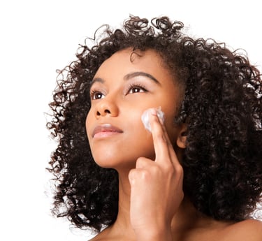 woman with curly hair applying ori shea butter to her face