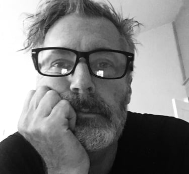 Black and white portrait of a man with glasses and a beard resting his chin on his hand.
