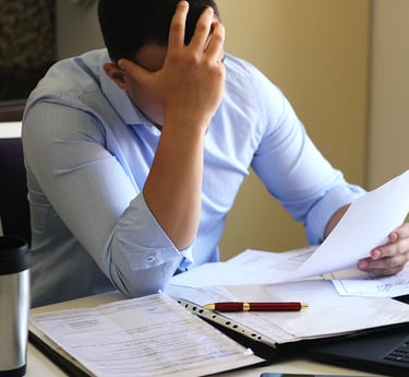 um homem em frente a papeis e com a mão no rosto em postura de preocupação