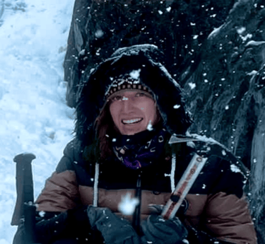 Smiling woman holding an ice axe while winter hiking and mountain climbing in the snow.