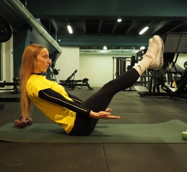 Una donna in maglia gialla esegue l'esercizio 'boat pose' su un tappetino da yoga in palestra, concentrandosi sull'equilibrio