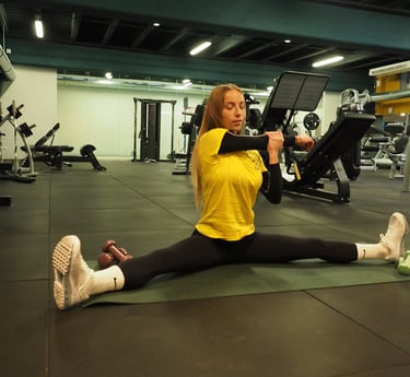 Una donna in maglia gialla esegue uno stretching in spaccata seduta, allungando il braccio per un esercizio di mobilità,