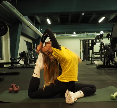 Una donna indossa una maglietta gialla con leggings neri e calze bianche mentre esegue una complessa posa yoga su un tappetin