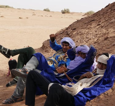 Three nomad guides in traditional dress lie down in a sand dune in the Moroccan Sahara desert