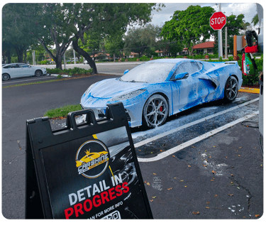 A blue Chevrolet Corvette C8 covered in white foam during a professional mobile car detailing service.