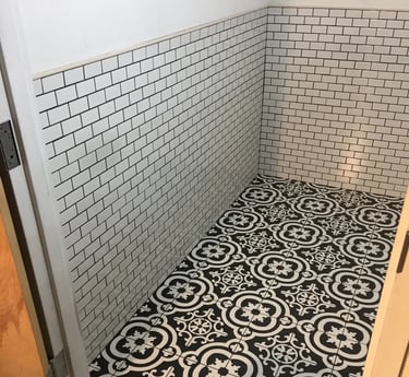 Black and white patterned floor tile installed in a half bathroom with white subway tile walls.