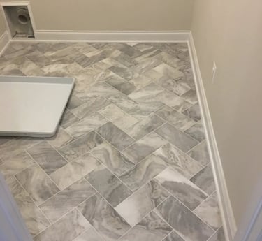 Gray marble-look porcelain tile installed in a herringbone pattern in a laundry room.