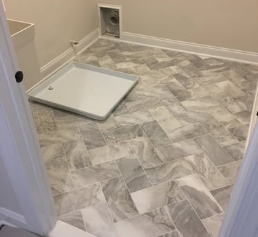 Gray marble-look porcelain tile installed in a herringbone pattern in a laundry room.