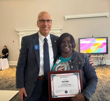 Kenya Wade smiling while receiving her 2025 HER Fellows Program certificate award from a colleague.