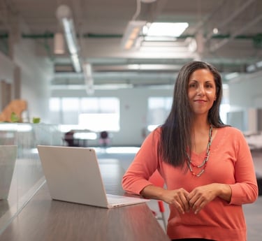 Professionelle Frau in einem modernen Büro, die an einem Stehtisch neben einem Laptop steht.