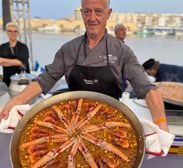 A chef presenting a large authentic Spanish seafood paella with langoustines and shrimp in a traditional pan.