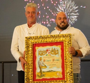 Two chefs proudly holding a gold-framed first prize award certificate for the best paella in the world.