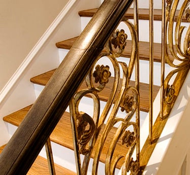 Elegant oak wood staircase featuring an ornamental gold wrought iron railing with floral scrollwork.