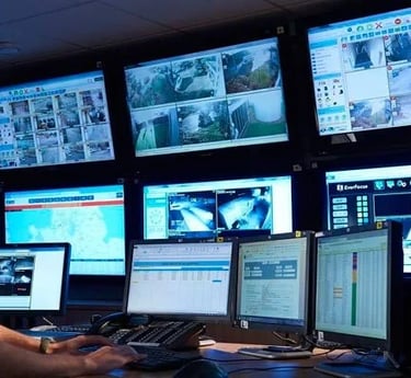 Security operator monitoring a multi-screen CCTV surveillance system in a modern control room.