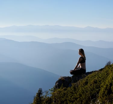Panoramic image of a mountainous environment with a young woman meditating in the foreground